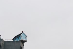 Photo of small blue house perched on edge of a cement dock.