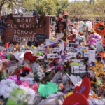 Austin-Statesman photo of the front of Robb Elementary School in Uvalde, Texas, the front lawn crowded with flowers and memorials.
