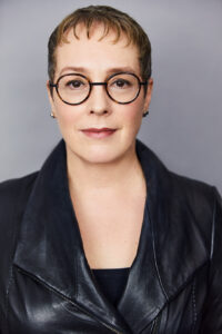 Headshot of Julia Angwin, a white woman wearing black leather jacket and glasses with dark-colored rims. 