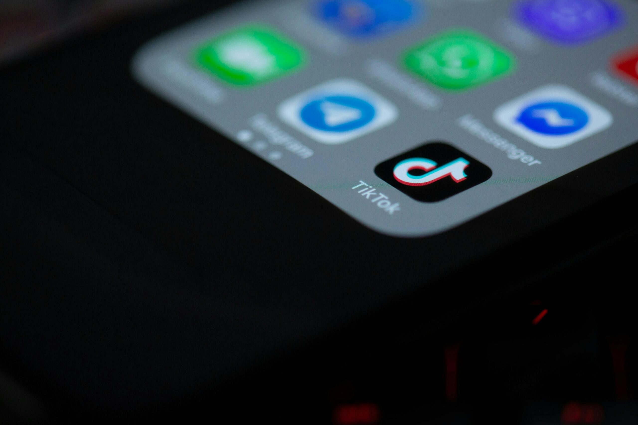 Photo of a cell phone lying on a black background, the TikTok app icon visible in the lower righthand corner of the phone.